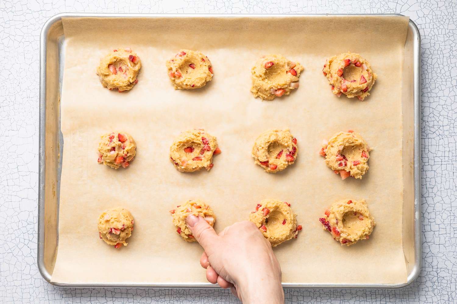 Thumb Creating Indents in the Strawberry Cheesecake Cookie Dough Dollops on a Parchment Paper Lined Baking Sheet