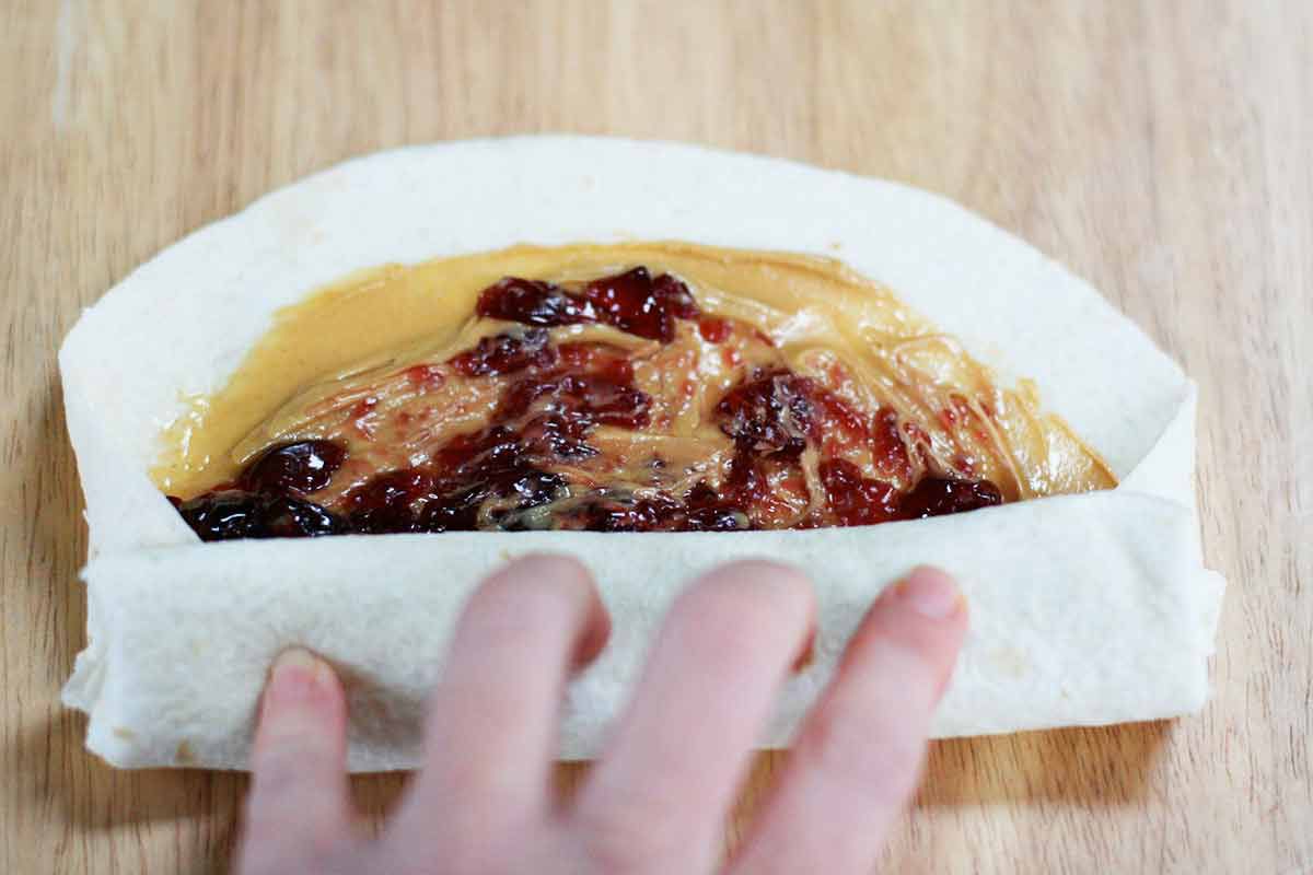 A child's hand rolling up a PB&J wrap