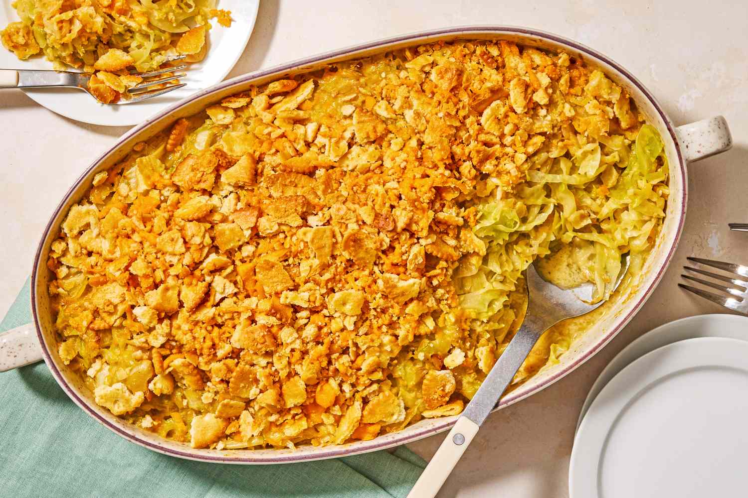 A casserole dish with cheesy cabbage casserole topped with a crunchy layer served with utensils and a green napkin nearby