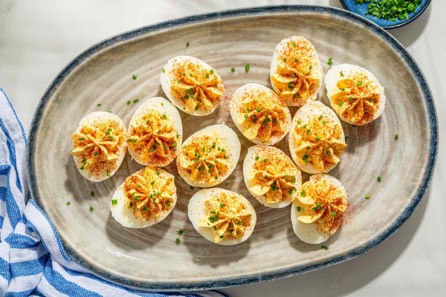 Overhead shot of a ceramic serving plate with deviled eggs, garnished with chopped chives and paprika