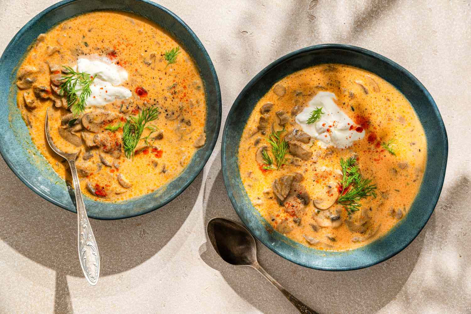 Two bowls with Hungarian mushroom soup, topped with sour cream, fresh dill, and smoked paprika