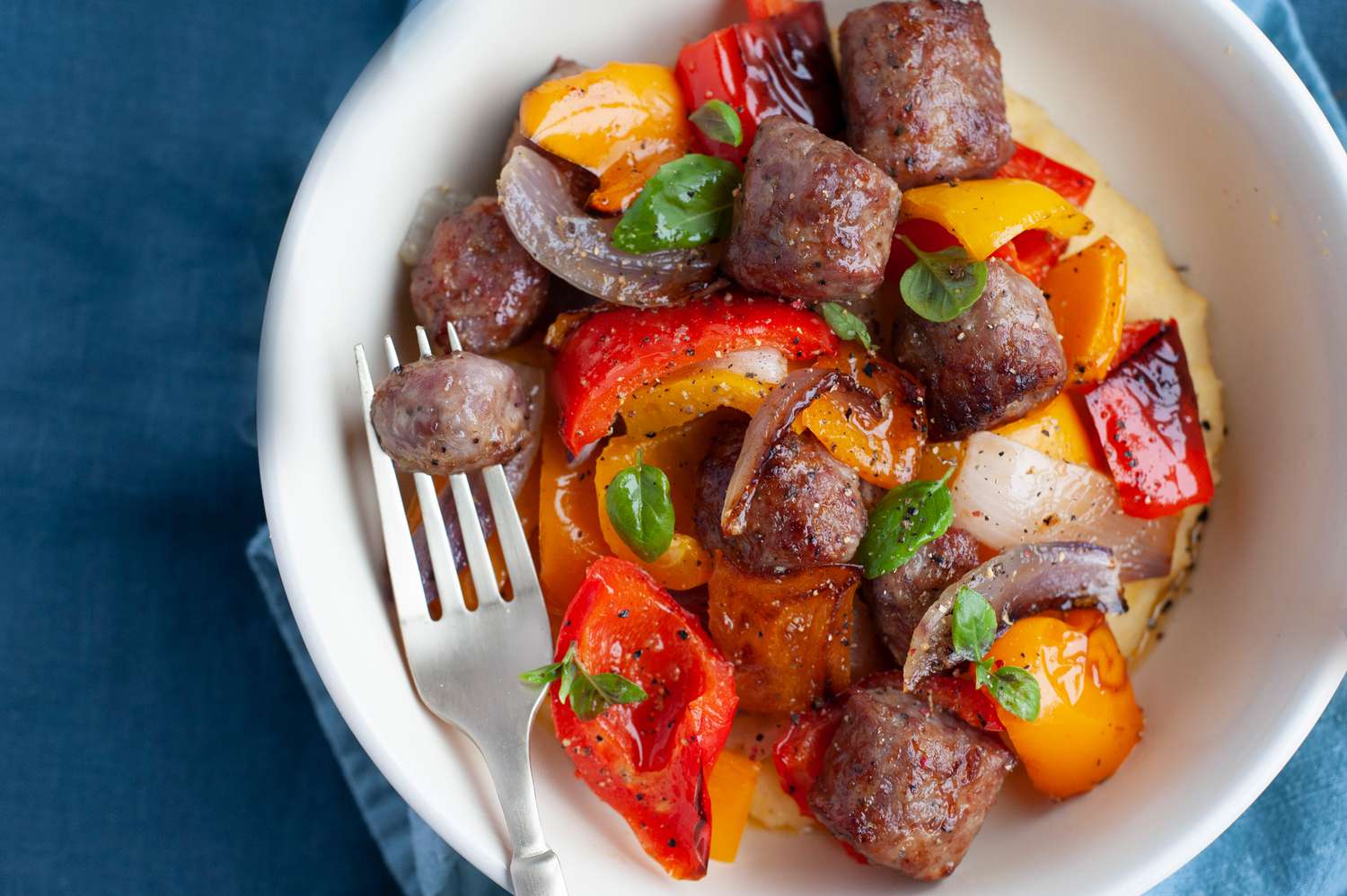 Sheet pan Italian sausage, peppers, and onions in a bowl with a fork.