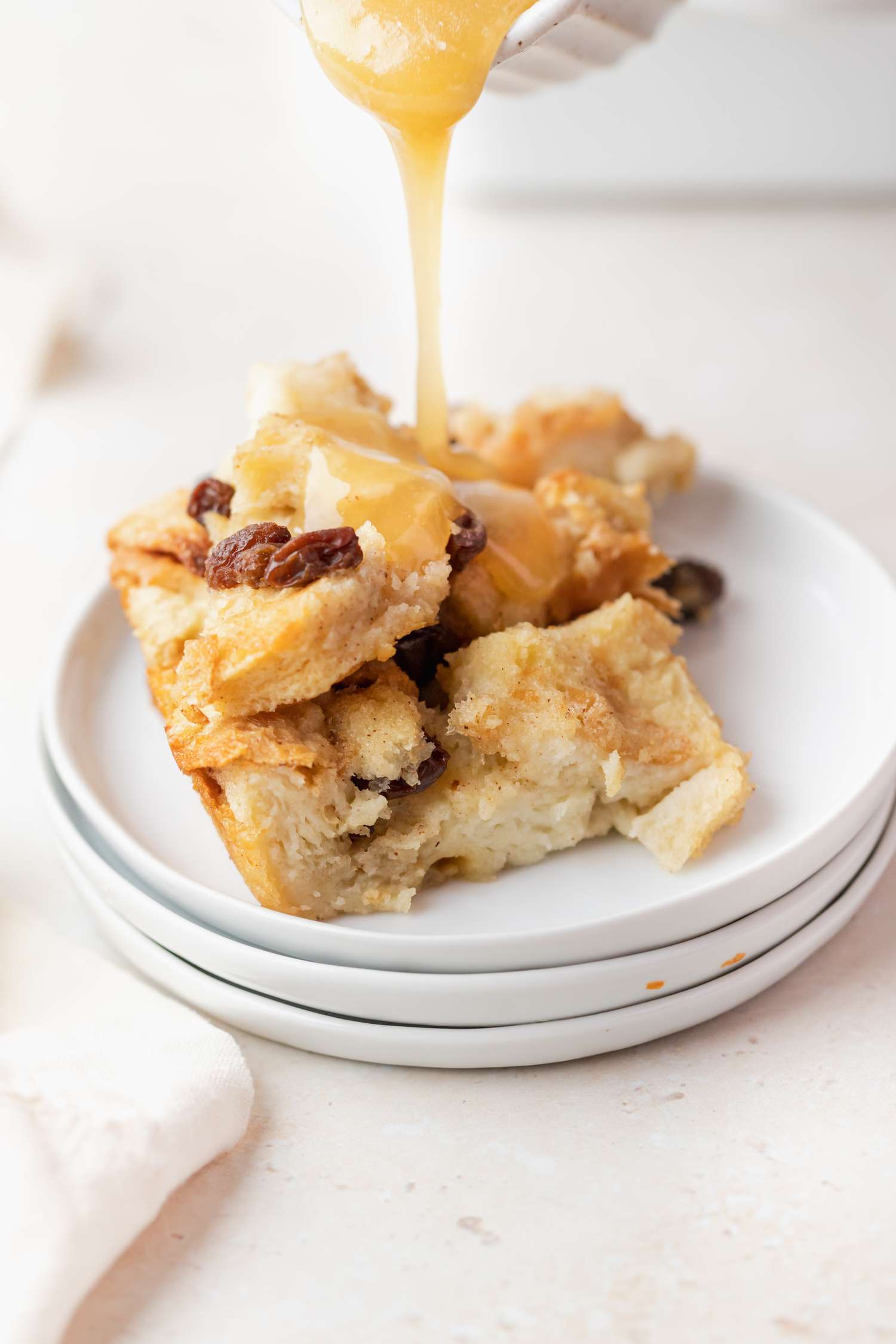 Pouring bread pudding sauce over a plate of bread pudding.
