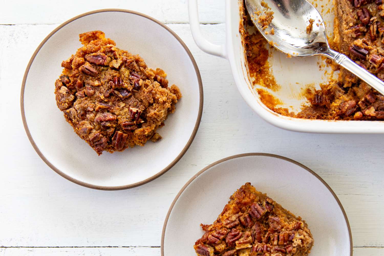 2 servings of Pumpkin Dump Cake on 2 plates, baking dish with remnants of the cake and a spoon