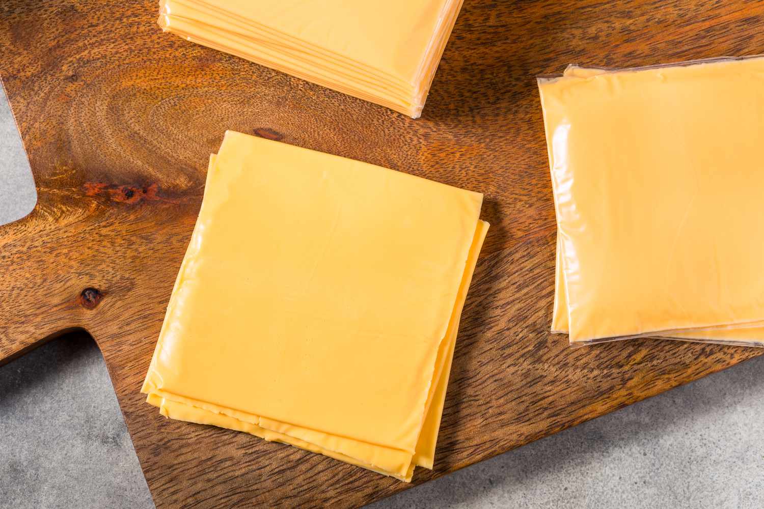 Sliced American cheese on a wooden cutting board, some wrapped in plastic.