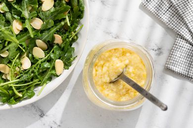 A glass jar with Whole Lemon Dressing next to a plate with a green arugula salad with chopped almonds