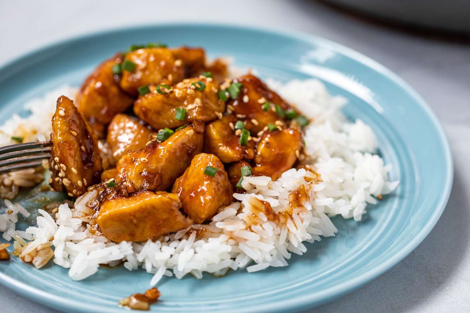 Side view of The BEST Bourbon Chicken Recipe served on a blue plate with rice.
