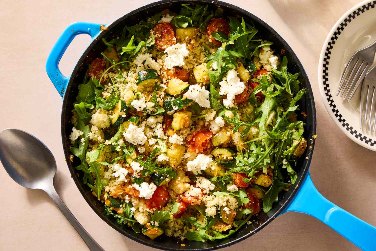 A skillet with couscous, vegetables, and goat cheese, garnished with greens and ready to serve