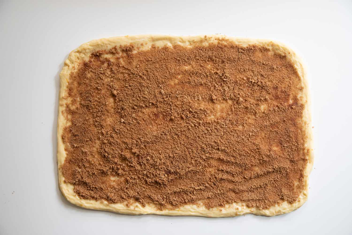 Dough rolled out and covered in cinnamon mixture to make a sticky buns recipe.