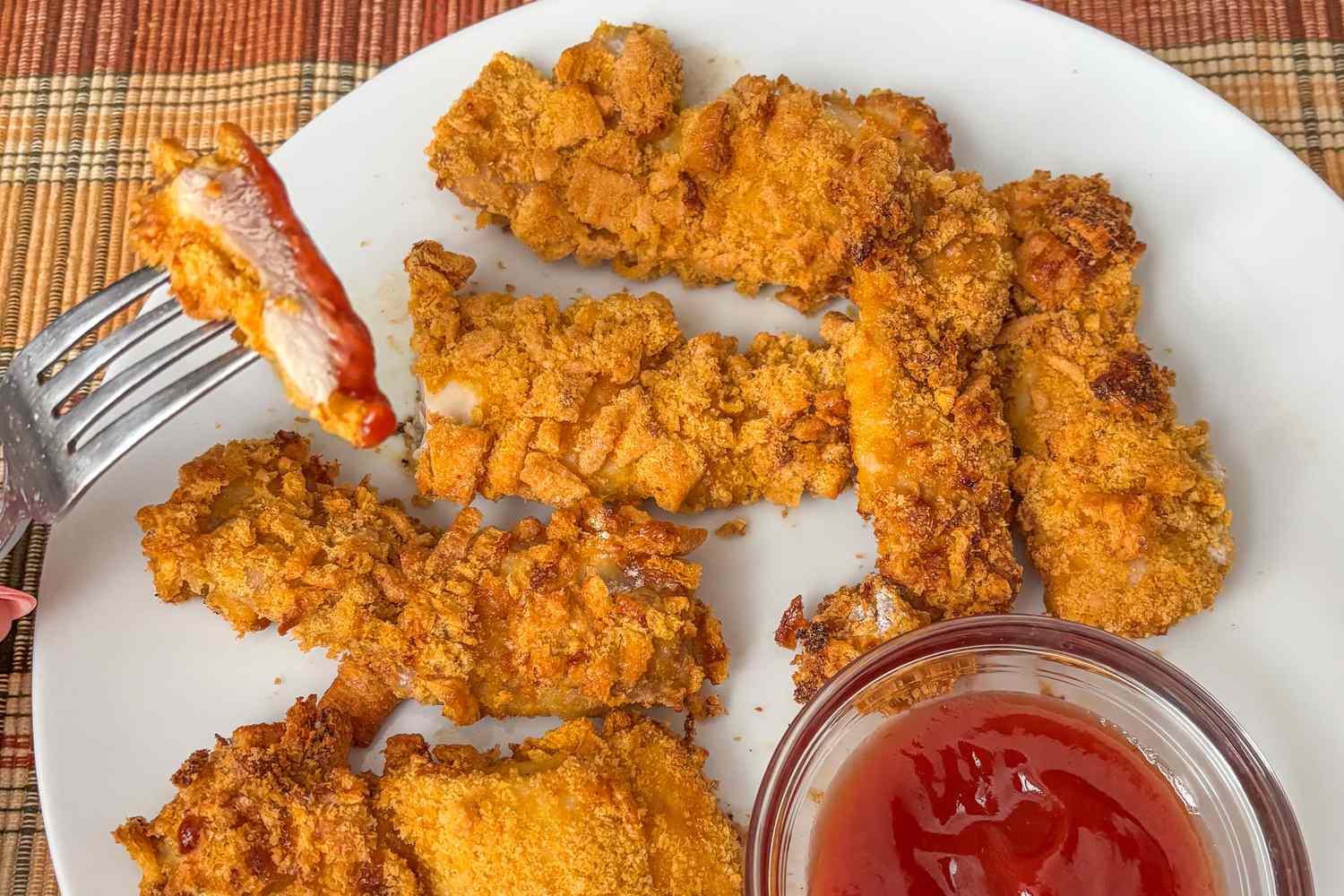 Ree Drummond's 4-Ingredient Chicken Strips on a plate with a side of ketchup, one bite forked and dipped