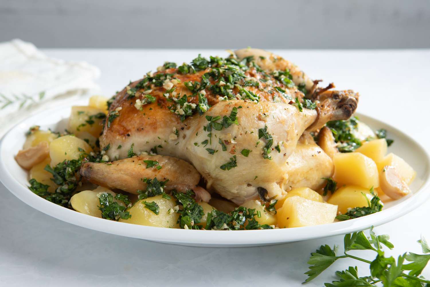 A roasted chicken garnished with herbs and surrounded by potatoes on a white plate