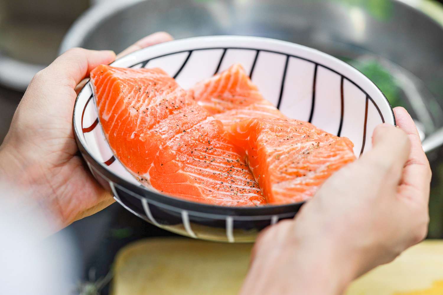 someone holding a bowl of seasoned salmon fillets 
