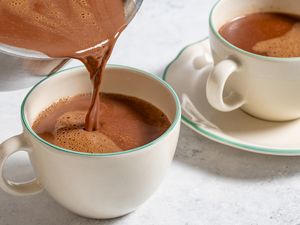 Pouring hot chocolate into a cup with another filled cup in the background