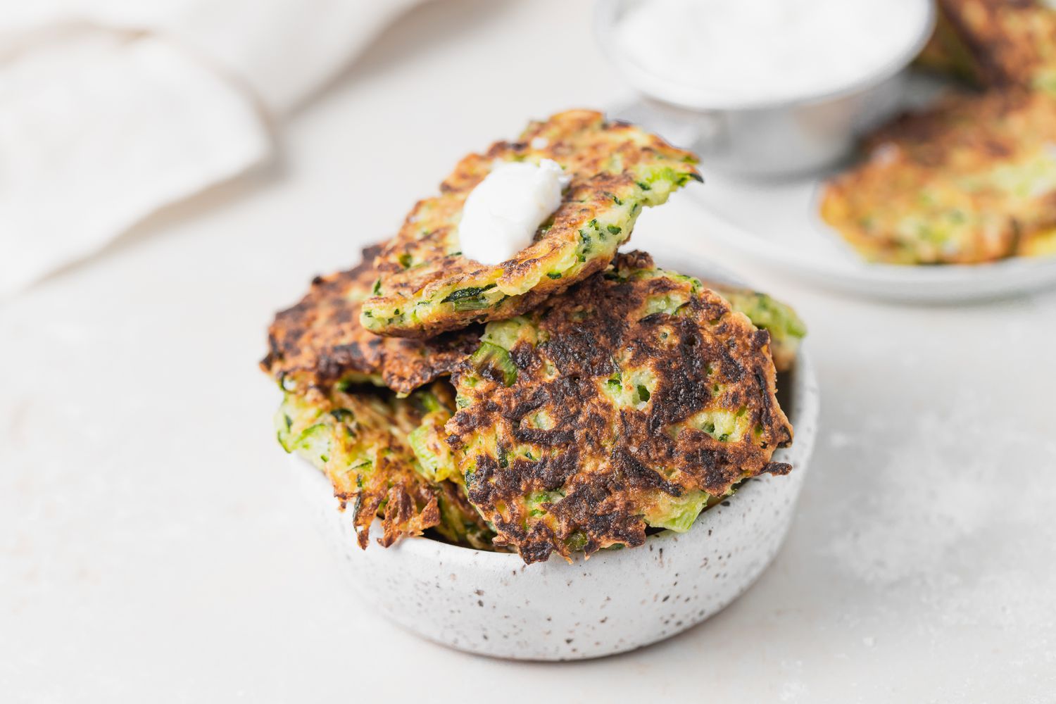 A bowl of zucchini fritters set on a white background.