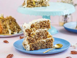 Side view of a blue plate with a tall slice of southern hummingbird cake and a cake on a cake stand behind it.