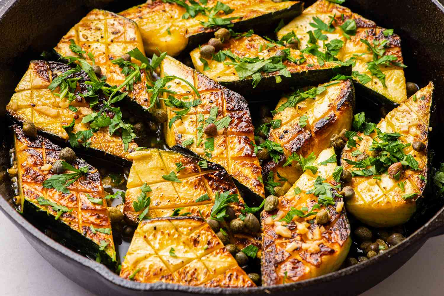 Sautéed zucchini pieces in a skillet garnished with herbs and capers