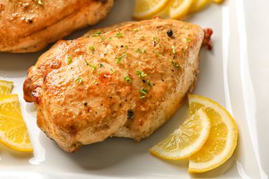 Closeup view of a roasted chicken breast with lemon slices on a white plate