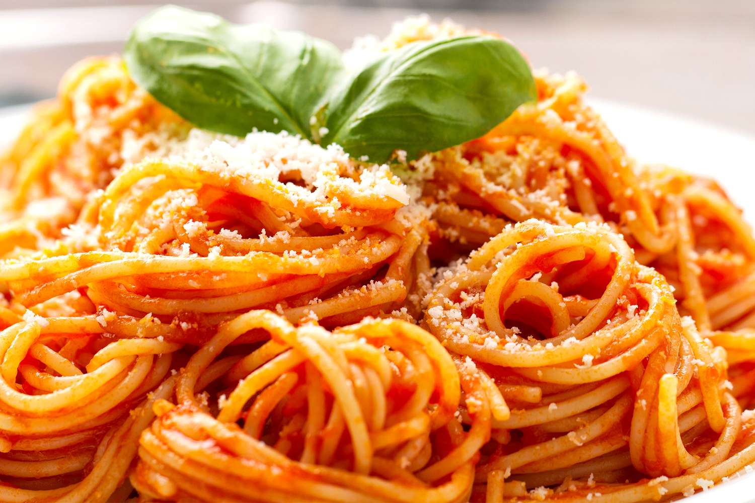 Plate of spaghetti with tomato sauce garnished with basil leaves and grated cheese