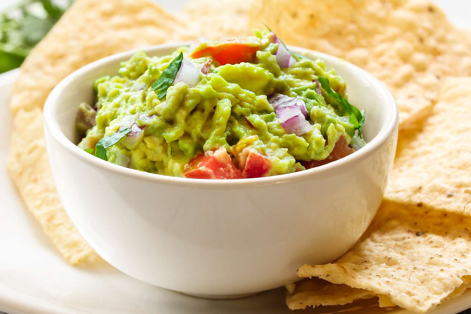 Fresh guacamole in a small white bowl with tortilla chips surrounding it