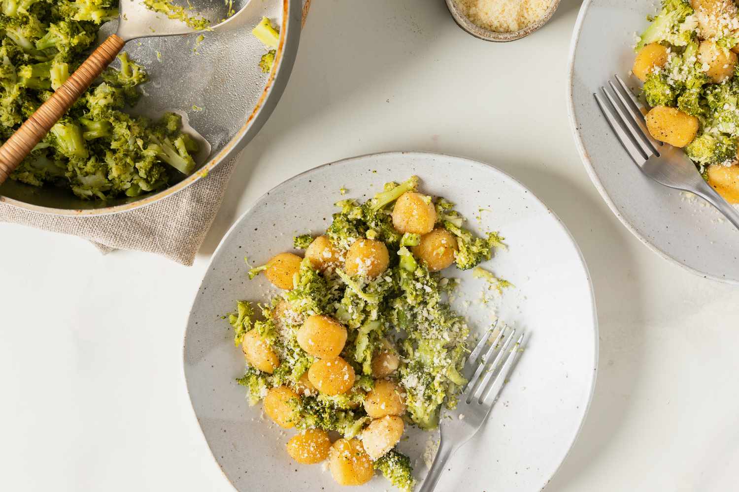 Plated gnocchi with broccoli sauce and grated topping with other servings visible