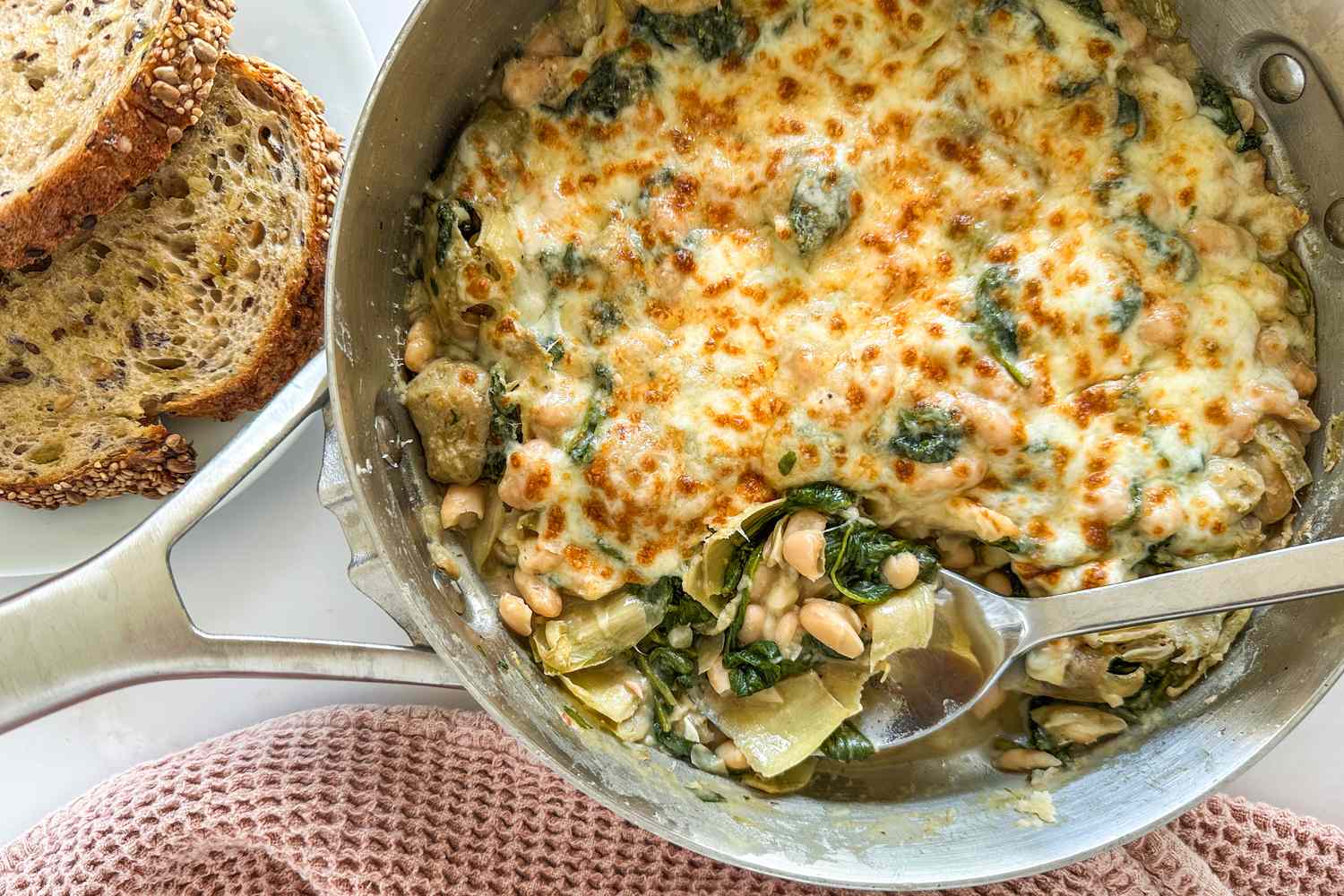 Baked spinach artichoke white bean dish in a skillet with toasted bread on the side