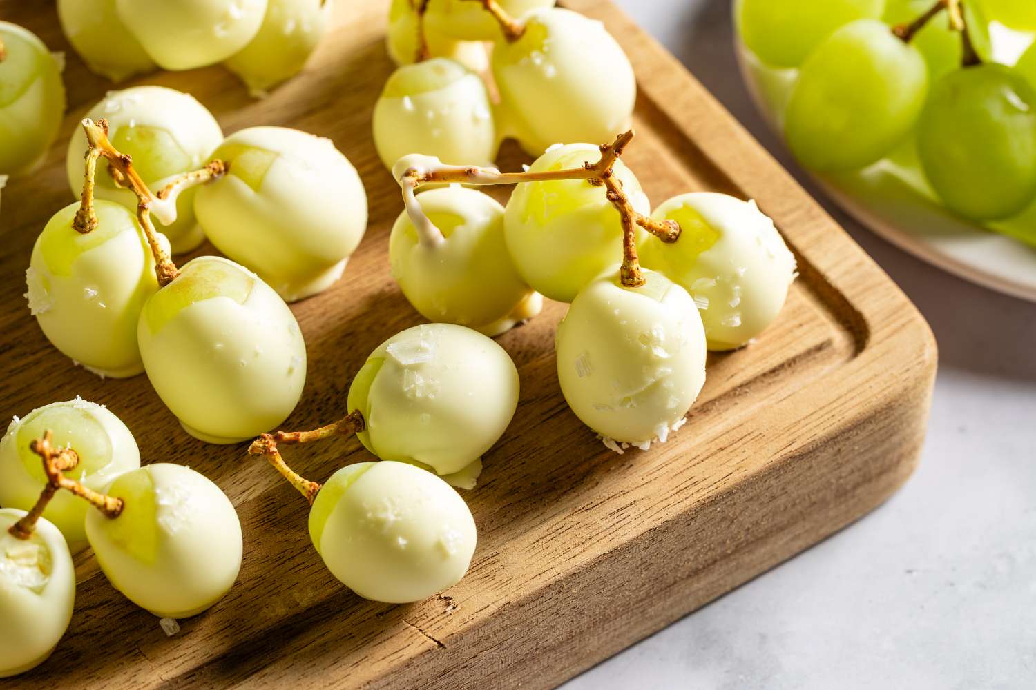 Closeup view of white chocolate covered green grapes on a wooden cutting board on a gray countertop