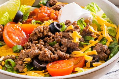A bowl of taco salad garnished with sliced black olives and sour cream
