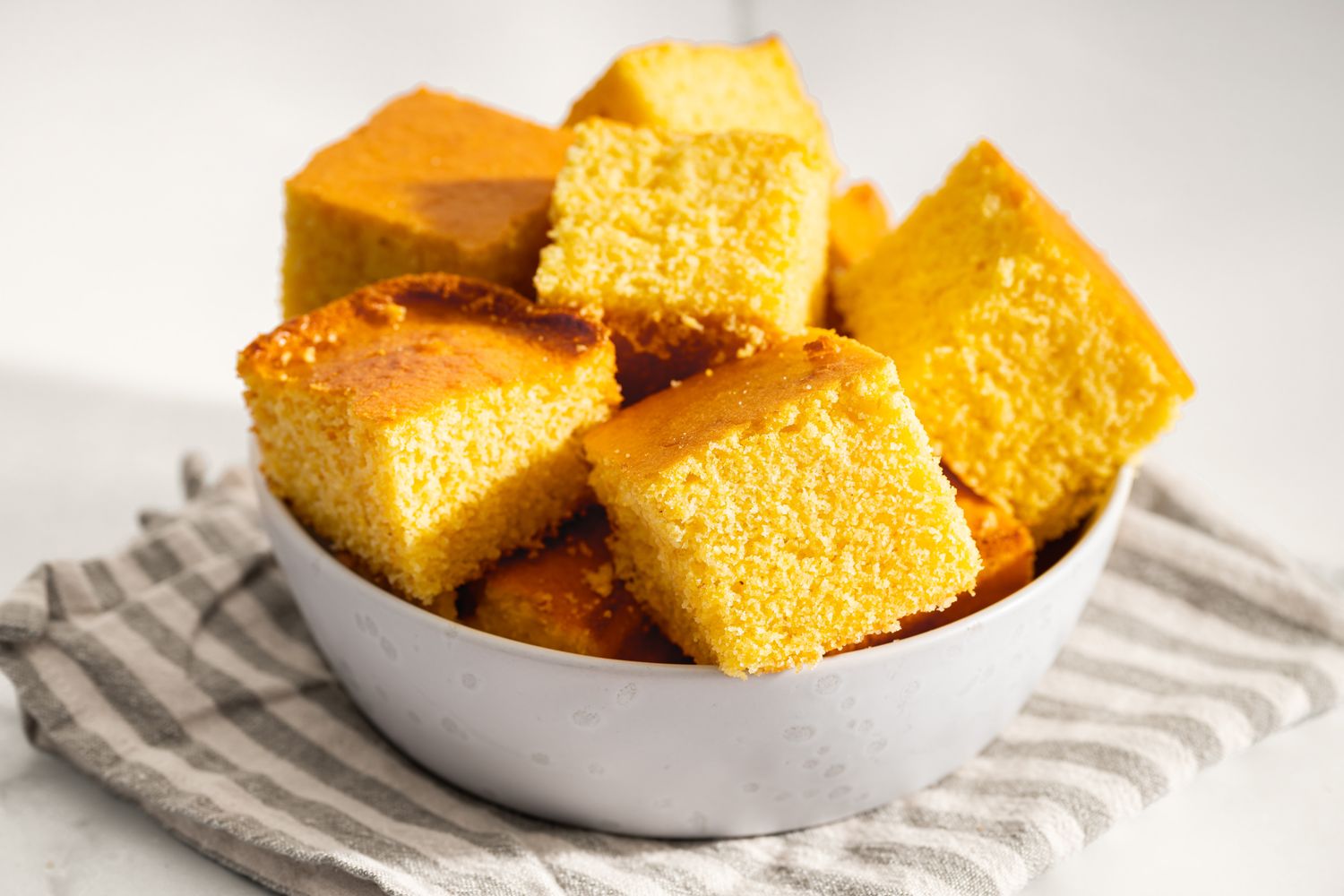 Bowl of squarecut cornbread pieces on a striped cloth