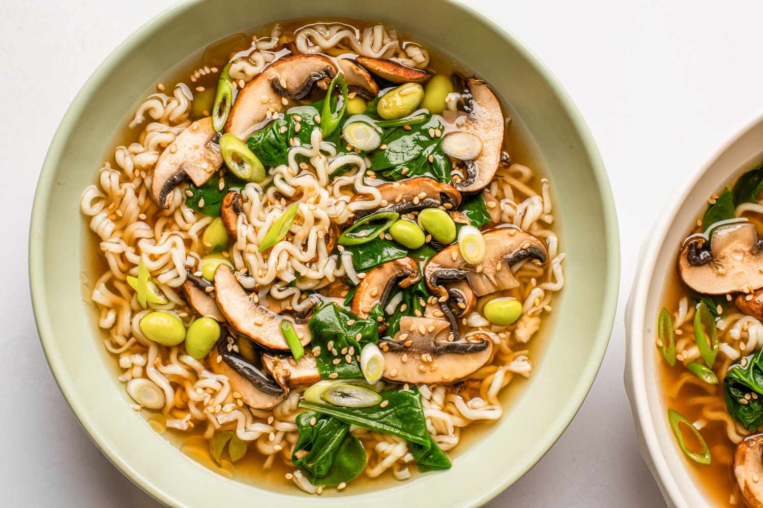 A bowl of noodle soup featuring mushrooms spinach edamame and scallions