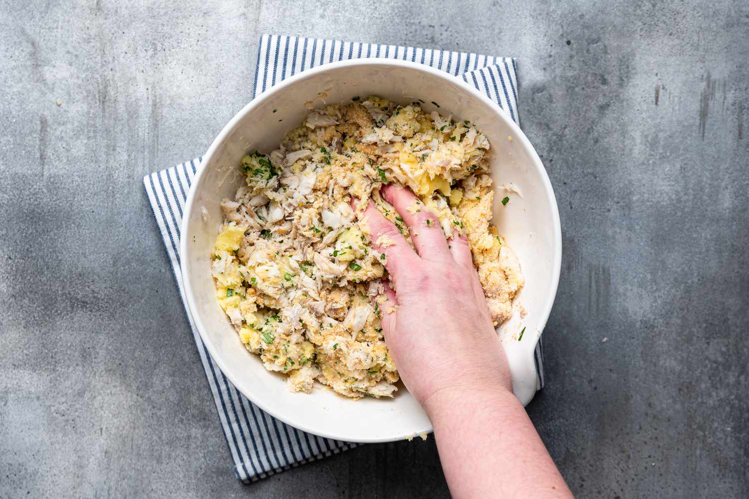 Ingredients for Cod Fish Cakes mixed in a bowl with a hand ready to form the cakes