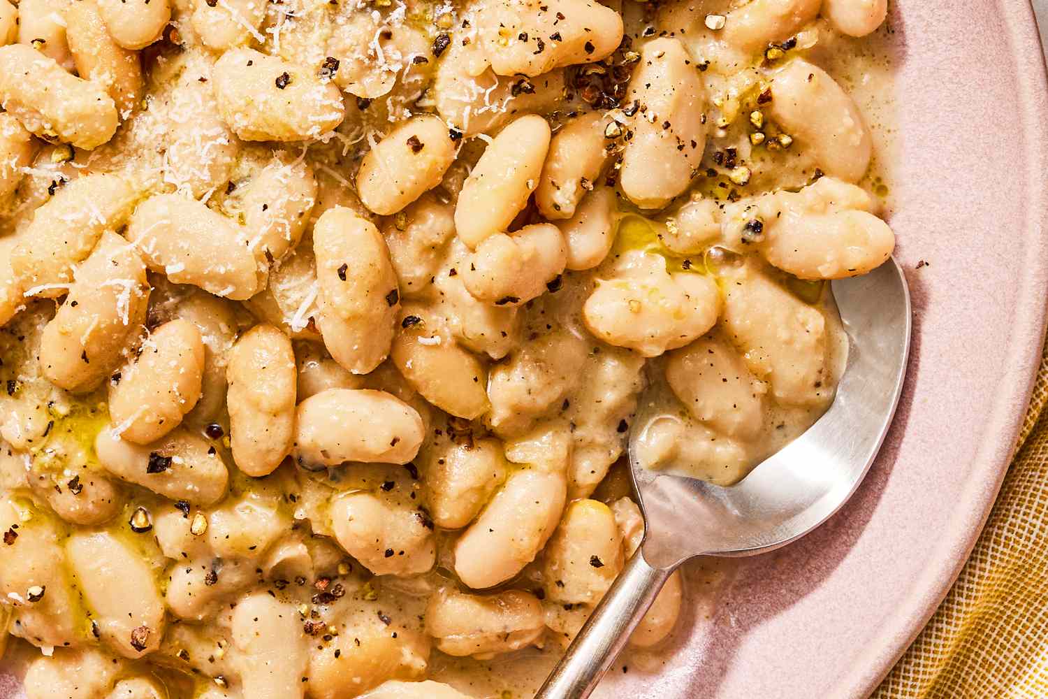 Cooked beans served on a plate accompanied by a sauce and garnished with cracked pepper