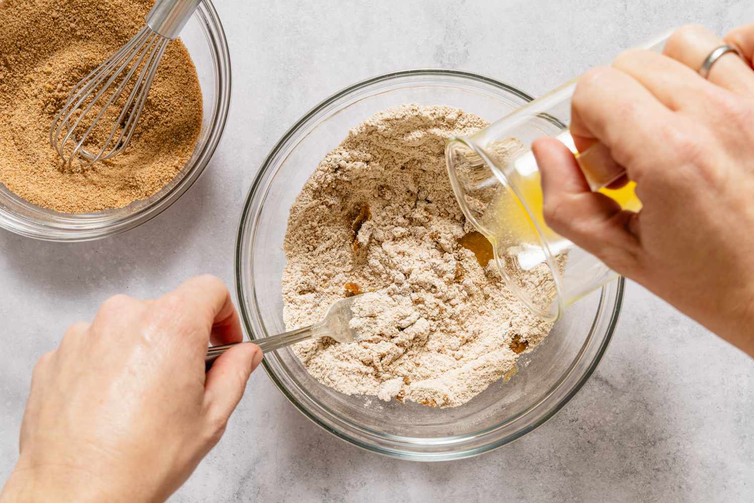 Mixing dry ingredients in a bowl with wet ingredients being poured from a small container