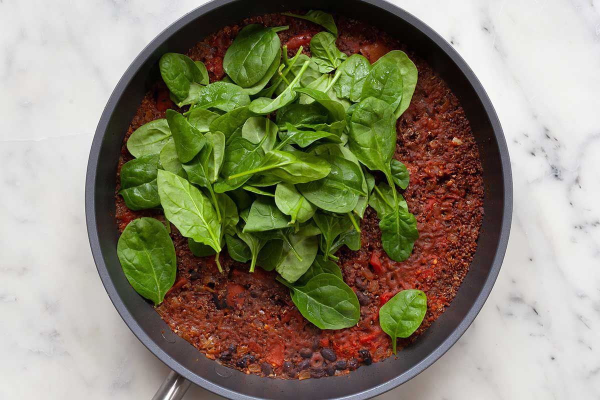 Saute pan with mexican-style black bean skillet dinner in it and spinach on the top.