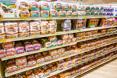 Shelves filled with various brands and types of packaged bread in a grocery store