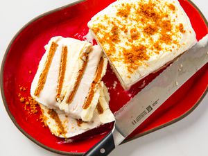 A biscoff ice cream cake served on a red plate, partially sliced with a knife visible