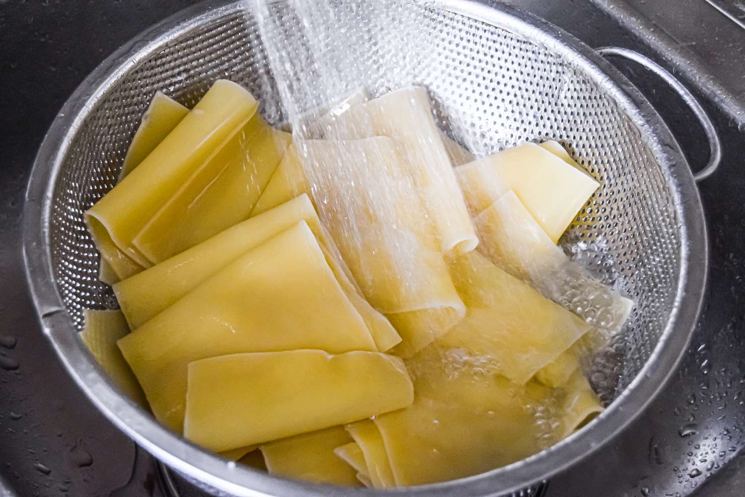 Cooked Lasagna Noodles in a Colander Being Rinsed in a Sink 