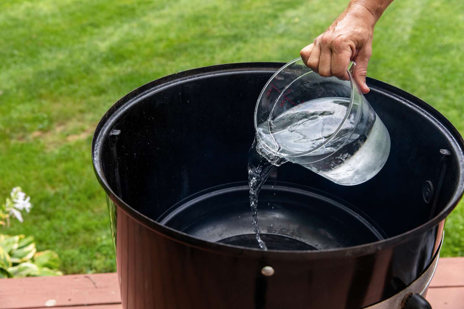 Adding water to a pan in a smoker to make pecan wood smoked turkey.