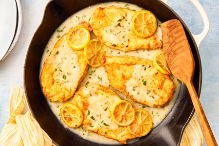 Chicken Francese in a skillet with a wooden spatula