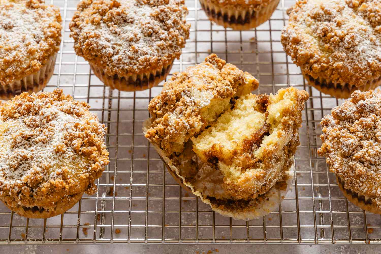 Coffee cake muffins on a cooling rack with one muffin split open