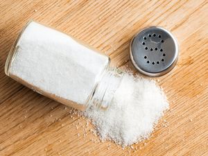 A spilled salt shaker with salt on a wooden surface