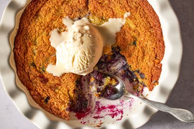 Blueberry corn cake with a scoop of vanilla ice cream on top in a fluted baking dish, served with a spoon