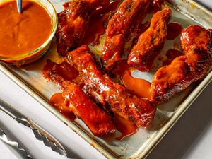 Saucy country-style ribs and a small glass bowl of BBQ sauce with a spoon on a baking sheet pan 