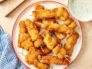 City Chicken, cooked and on skewers on a plate with a creamy sauce on the side in a small bowl