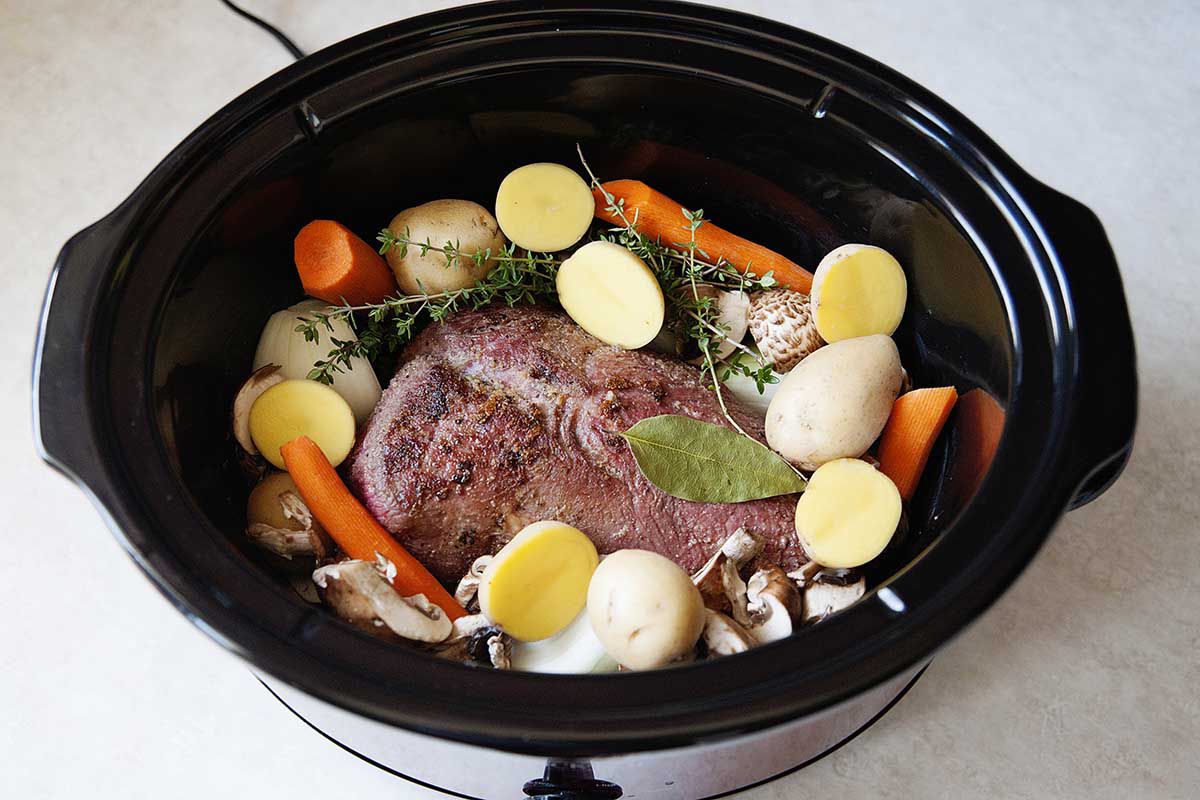 Pot Roast, Potatoes, herbs and carrots in a slow cooker.