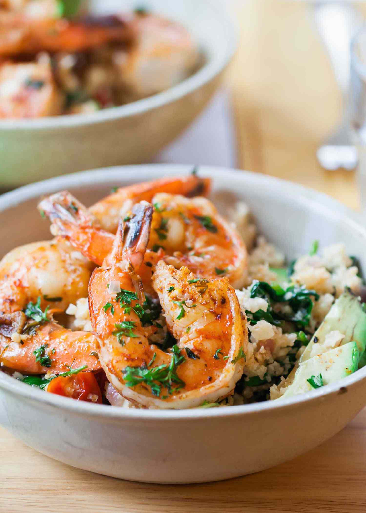 Shrimp and cauliflower rice in a white bowl with herbs and avocado sices. A second bowl identical bowl is in the background.