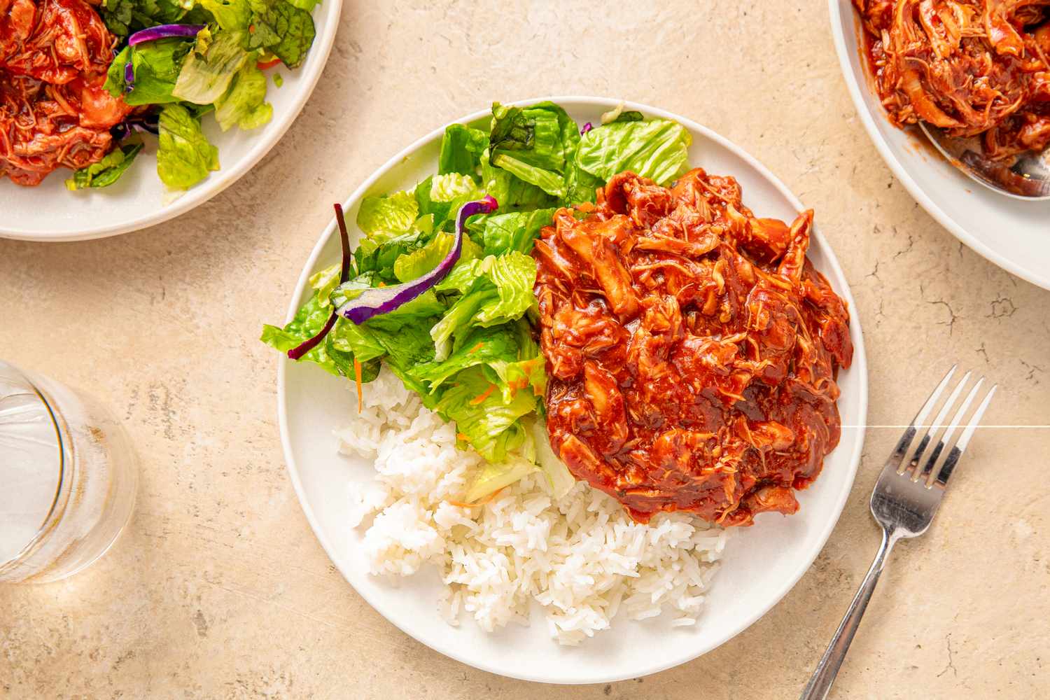 A plate of slowcooked BBQ chicken served with white rice and a side salad presented on a table