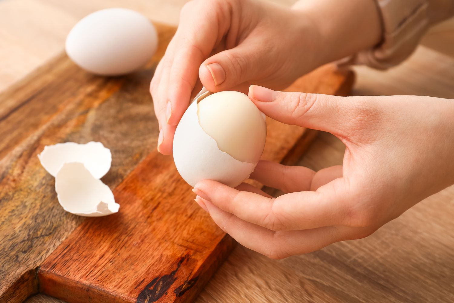 Woman peeling boiled egg at wooden table, closeup