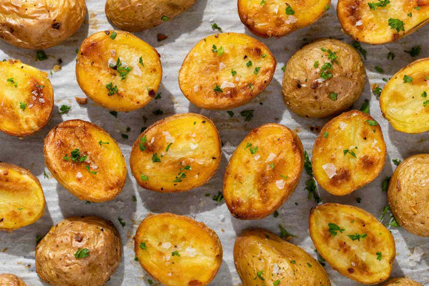 Roasted halved potatoes on a baking sheet, sprinkled with flakey salt and parsley