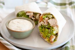 Chicken Caesar Wraps Cut in Half on a Plate with a Small Bowl of Dressing