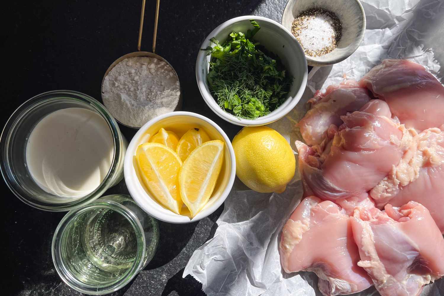 Ingredients for a recipe including raw chicken lemon wedges fresh herbs salt flour milk and oil arranged on a surface